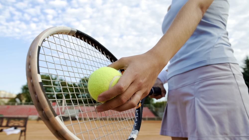 Photograph of woman holding tennis ball preparing to serve.